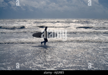 Un surfeur solitaire marchant le long de la plage en hiver. Camber Sands, East Sussex, Angleterre Banque D'Images