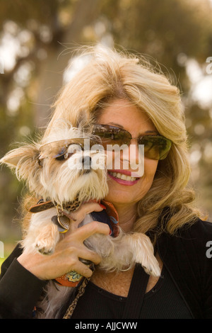 Une femme d'âge moyen des sourires et détient son bien-aimé petit chien. Les deux sont le port de lunettes. Banque D'Images