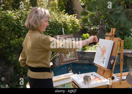 Une femme debout devant un chevalet, bénéficie d'la peinture de plein air dans un jardin de banlieue. Banque D'Images