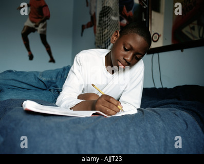 Boy doing homework on bed Banque D'Images