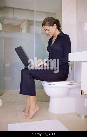 Femme assise sur une toilette à l'aide d'un ordinateur portable Banque D'Images