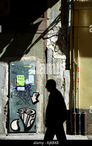 Silhouette de vieil homme contre la lumière du soleil en passant devant la porte en métal peint avec des graffitis dans une rue latérale, Valencia Espagne Banque D'Images