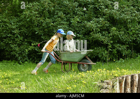 Déménagement fille son frère dans une main barrow dans le jardin Banque D'Images