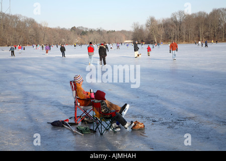 Les femmes et les jeunes en premier plan l'enfant assis sur deux chaises pliantes sur la glace en regardant les patineurs Banque D'Images