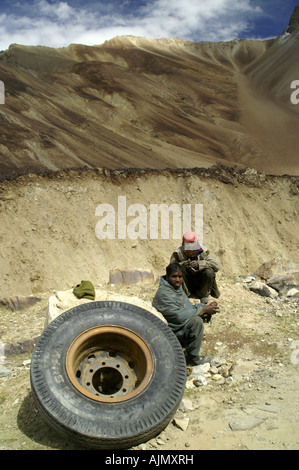 Les indiens isolés homme assis avec d'énormes roues pneus de camions en région isolée du Ladakh Himalaya sur la route de Manali à Leh. L'Inde. Banque D'Images