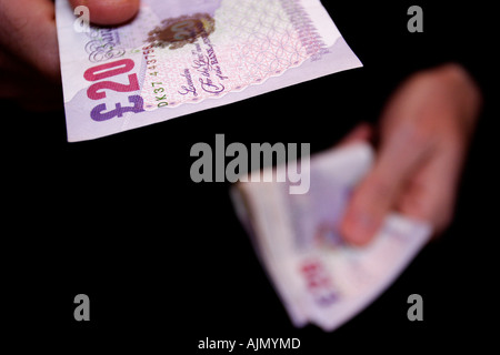 Un homme de main au cours d'une vingtaine de British pound note à partir d'un ensemble d'espèces proches de culture mains sur fond noir Banque D'Images