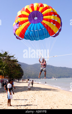 Les terres d'un homme après le parachute ascensionnel sur la plage de Batu Ferringhi, l'île de Penang, en Malaisie. Banque D'Images