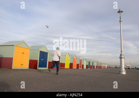 Homme court passé peint de couleurs vives, des cabines de plage sur le front de mer de Brighton Banque D'Images
