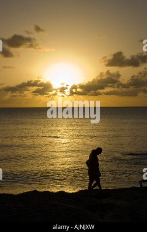 Couple en train de marcher sur une plage des Caraïbes silhouetté contre le soleil couchant Banque D'Images