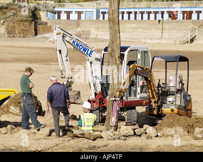 Trois ouvriers à l'aide de machines de l'usine de sortir un post sur une plage de sable. Banque D'Images