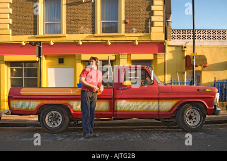 Homme debout par red Ford F100 camionnette avec un bâtiment jaune et rouge vif à l'arrière-plan Banque D'Images