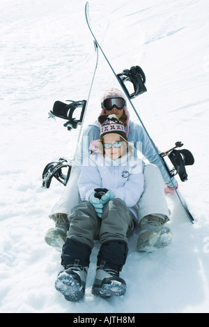 Deux jeunes skieurs assis sous les skis ensemble, smiling at camera, portrait Banque D'Images