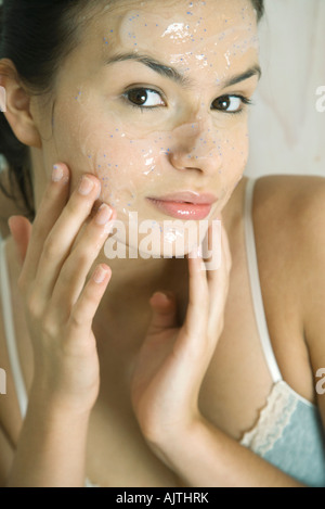 Jeune femme mettre masque exfoliant sur le visage, smiling at camera Banque D'Images
