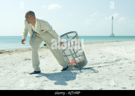 Man pulling poubelle à sunny beach, pleine longueur Banque D'Images