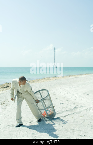 Man pulling poubelle à sunny beach, retour sur toute la longueur de l'épaule, Banque D'Images