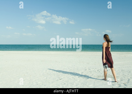 Femme marchant sur la plage, exerçant son récipient transparent, pleine longueur, vue arrière Banque D'Images