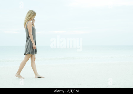 Young woman walking on beach, using cell phone, pleine longueur Banque D'Images