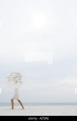 Woman standing on beach, haut du corps caché par parasol, pleine longueur, side view Banque D'Images