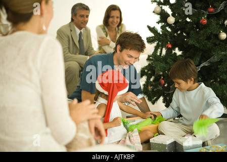 Le père et les deux enfants assis par arbre de Noël, l'ouverture présente ensemble, à regarder en famille Banque D'Images