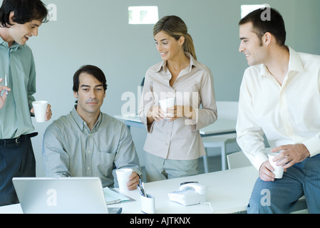 Les associés se sont réunis autour de collègue assis à l'ordinateur portable, toutes les tasses jetables holding Banque D'Images