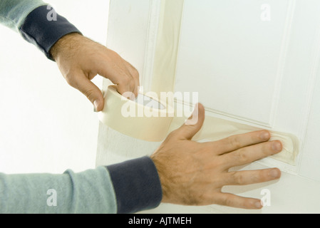 L'homme de mettre du ruban de masquage sur la porte en bois, close-up of hands Banque D'Images