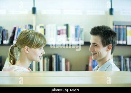 Les étudiants masculins et féminins face à face en bibliothèque, smiling at each other
