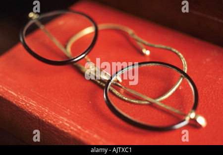 Une paire de lunettes avec lentilles circulaires et fine écaille de frames et armes fil couché sur un livre rouge Banque D'Images