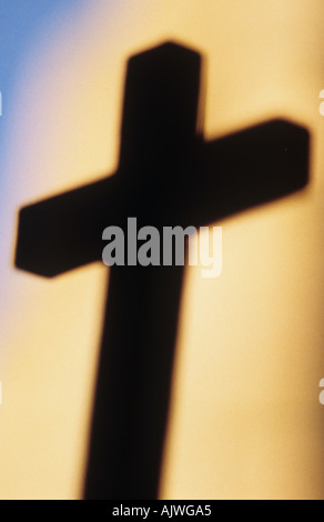 Crucifix impressionniste silhouetté contre un mur de pierre chaude dans lumière du soir avec ciel bleu au-delà Banque D'Images