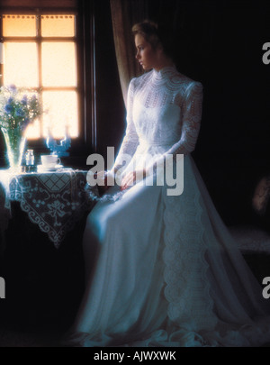 Jeune femme en blanc longue robe nuptiale assis par fenêtre. Banque D'Images