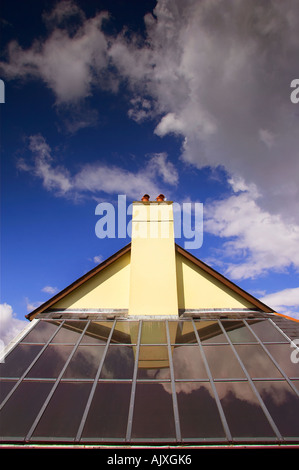 Des panneaux solaires sur un toit dans le Devon, UK, sous une toiture inclinée et la cheminée contre un ciel bleu avec des nuages. Banque D'Images