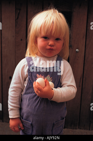 Les enfants. Portrait de petite fille blonde holding oeufs de poule nouvellement posées. Banque D'Images