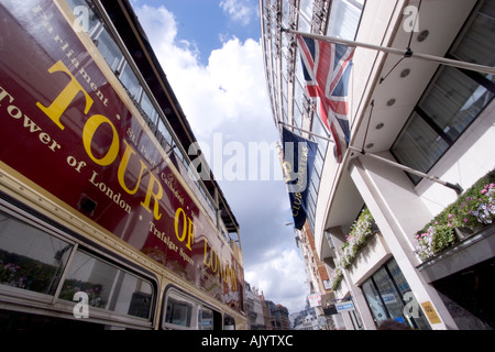 Visite à toit ouvert du bus touristique londonien avec drapeau union Jack flottant sur la façade du magasin Banque D'Images