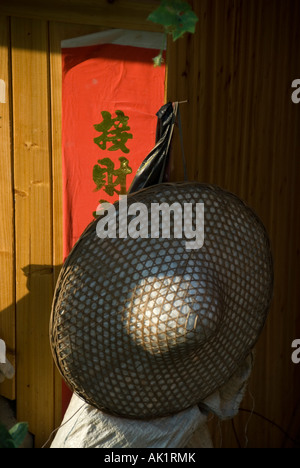 Recevoir la prospérité et fortune written derrière un chapeau de paille accroché à l'extérieur d'une maison en bois traditionnelle de la minorité Yao du sud de la Chine Banque D'Images