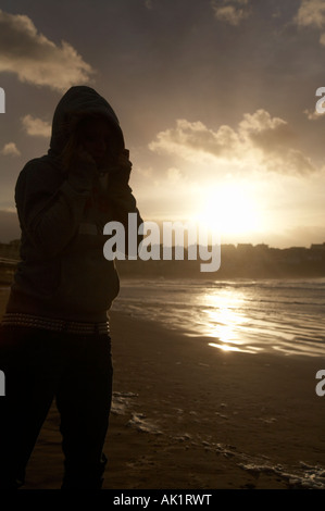 Les jeunes filles portant un sweat à capuche avec le capot en place debout sur une plage au coucher du soleil Banque D'Images