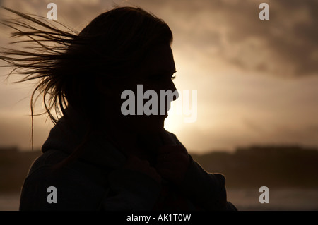 Silhouette of female student debout sur une plage au coucher du soleil avec les cheveux au vent Banque D'Images