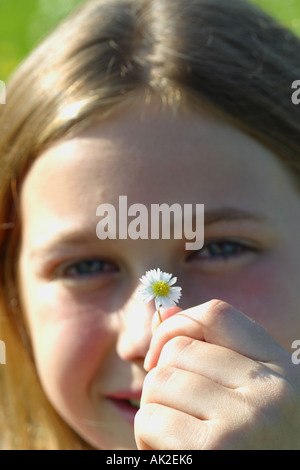 Jeune fille âgée de 12 ans tenant une petite fleur marguerite en face de son visage souriant Banque D'Images