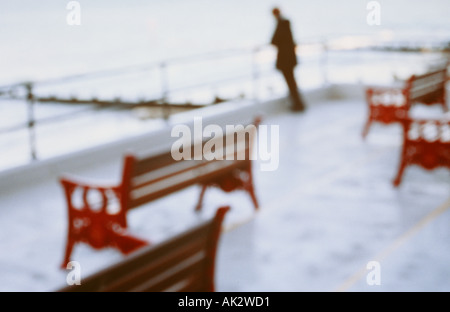 L'impressionniste figure appuyée sur les garde-corps entourant les banquettes vides et sur le calme de la mer d'hiver Banque D'Images