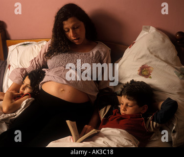 Une femme enceinte se lit à son fils et sa fille au lit, Londres, Royaume-Uni. Banque D'Images