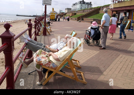 Couple de personnes âgées au soleil dans des chaises longues par le front de mer . Royaume-uni Bridlington Banque D'Images