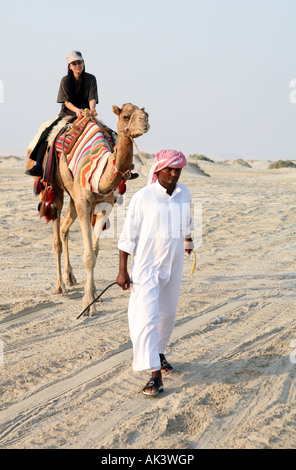 Une femme japonaise monte un chameau conduit par un bédouin dans le désert qatari à côté du Sealine Beach Resort Novembre 2007 Banque D'Images