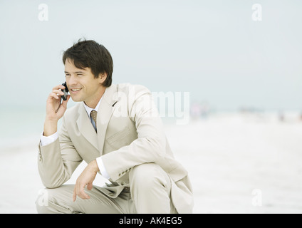 Woman crouching on beach, using cell phone Banque D'Images