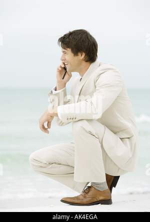 Woman crouching on beach, using cell phone Banque D'Images