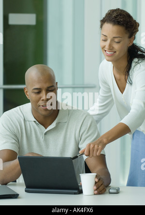 Femme penché sur l'épaule de l'homme, pointant sur un écran d'ordinateur portable Banque D'Images