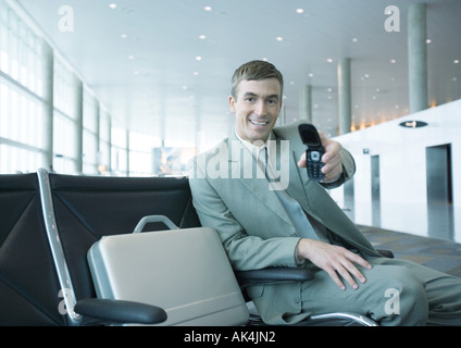 Businessman holding out cell phone in airport lounge Banque D'Images