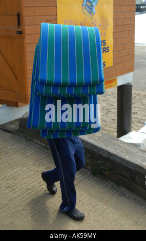 Un assistant de plage saisonnier d'été embauché transporte une pile de matelas de transats à placer sur les transats sur la plage de Shankill, juste avant les visiteurs Banque D'Images