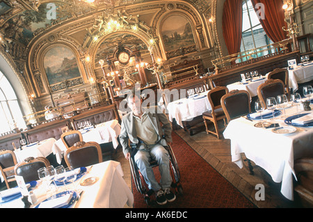 Homme handicapé en vacances au 'Restaurant Français' 'le train Bleu' en fauteuil roulant Paris France, ancienne Brasserie, accès spécial Banque D'Images