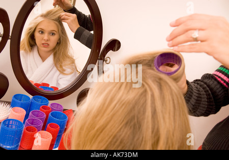 Maman de rouler les cheveux de Young Teen Girl (15-17) Fille, alors qu'elle se regarde dans le miroir USA Banque D'Images