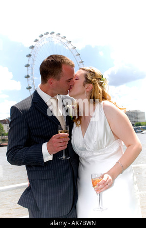 Les jeunes mariés fraîchement white couple kissing on boat holding glasses of champagne. London Eye en arrière-plan pendant les jours ensoleillés. Banque D'Images