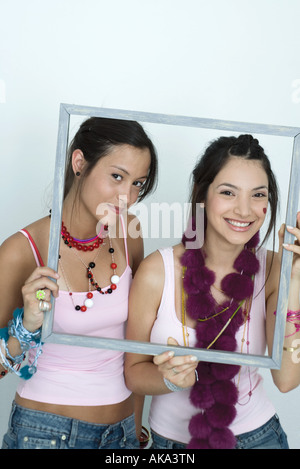 Deux jeunes femmes friends holding up photo frame, smiling at camera, portrait Banque D'Images