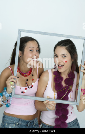 Deux jeunes femmes friends holding up photo frame, smiling at camera, portrait Banque D'Images